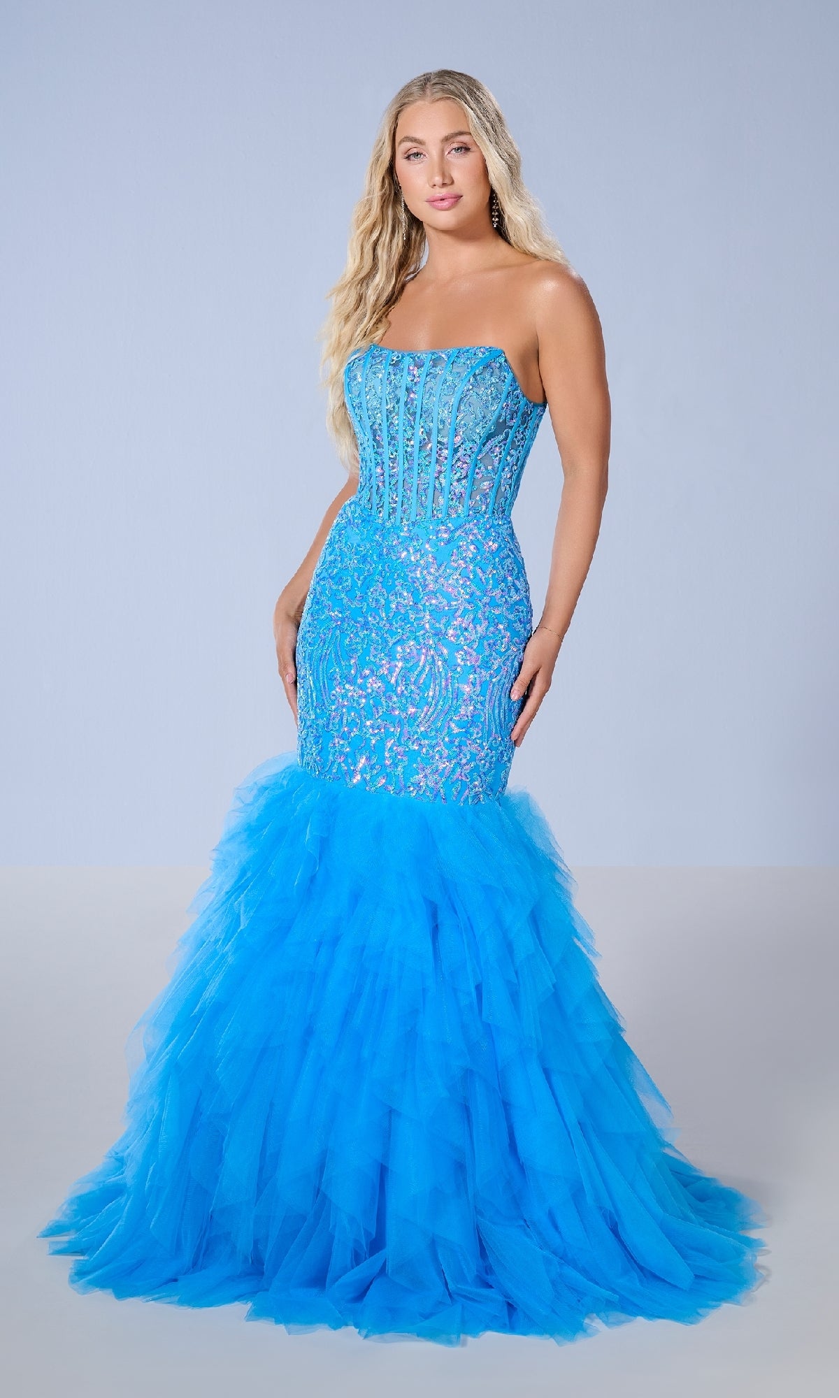 A woman wears the Tiffany 16165 long prom dress, featuring a strapless mermaid silhouette with a lace bodice and voluminous ruffle tulle skirt, standing against a plain light background.